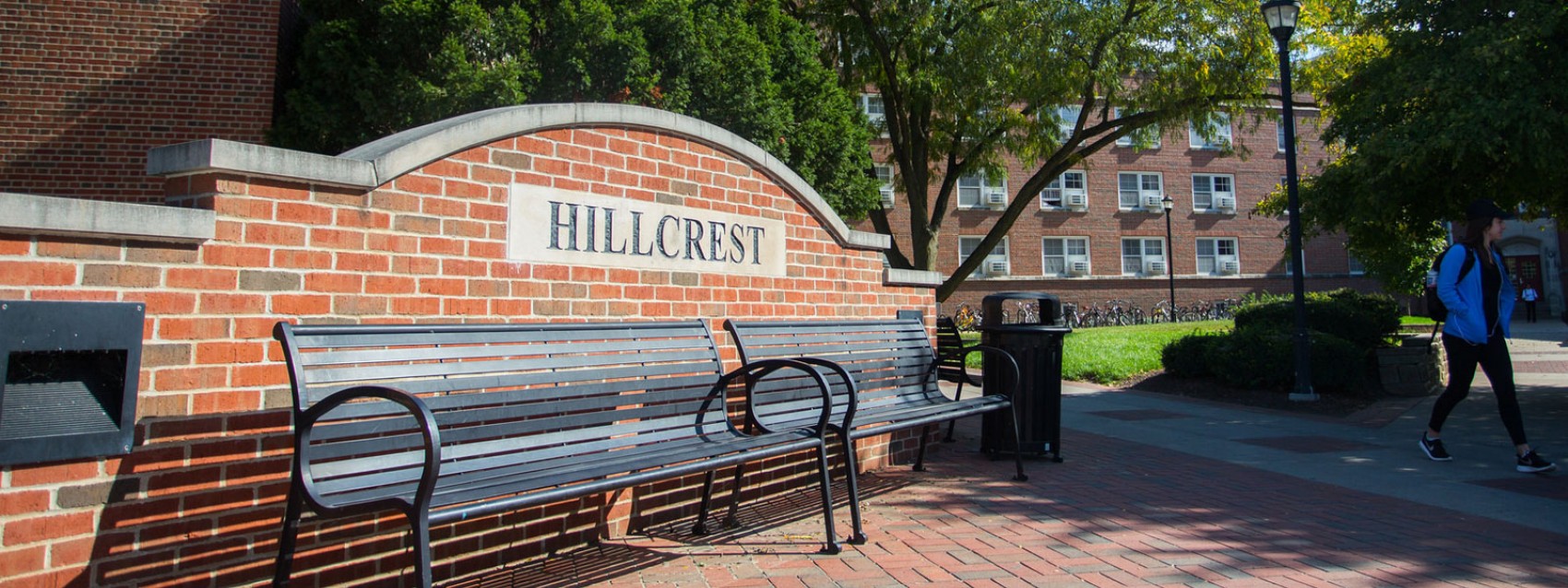 Hillcrest entrance with benches and students walking near the stone sign that contains the text 'Hillcrest'